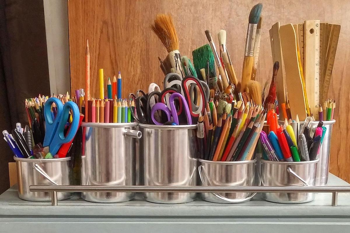 Various art supplies like pencils, brushes, and scissors organized in metal containers.