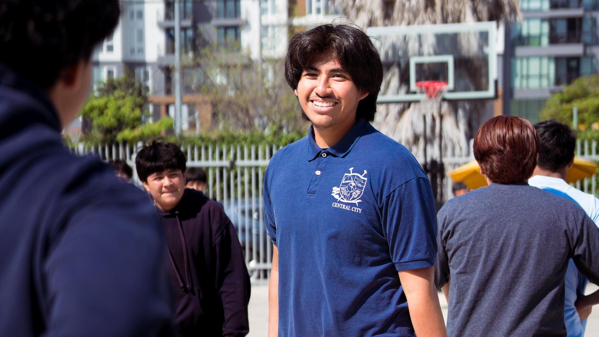 Students walk outside in casual clothing, some interacting in a schoolyard setting.