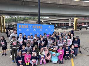 large group of students in athletic wear sitting in front of Kids of Steel sign