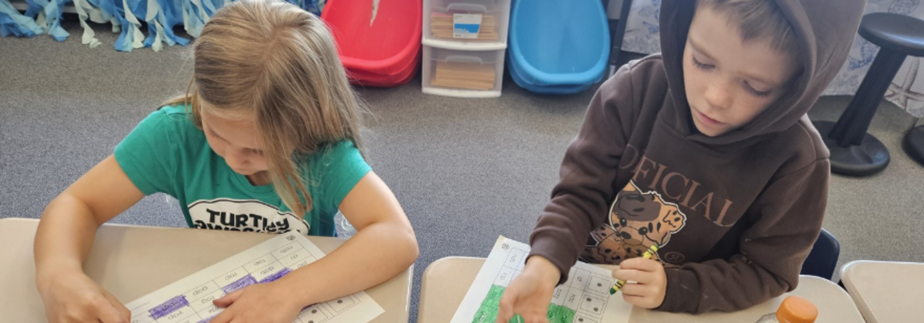 Two children coloring worksheets at a table, with a water bottle nearby.