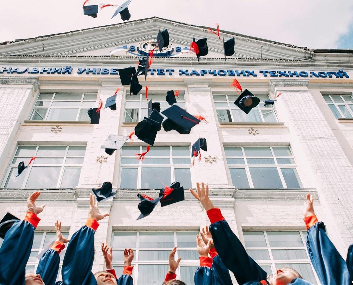 College students throwing their graduation caps in the air in front of a building