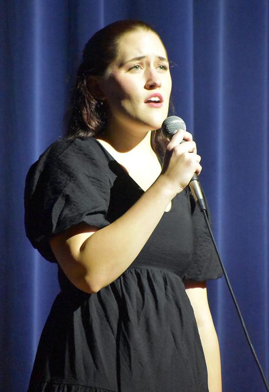 A woman in a black dress sings emotively into a microphone.