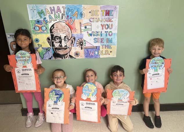 Students holding their artwork in front of mural.