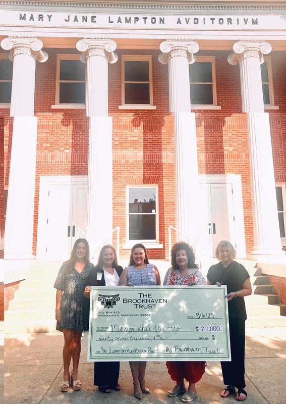 Five women holding a large check outside the Mary Jane Lampton Auditorium.
