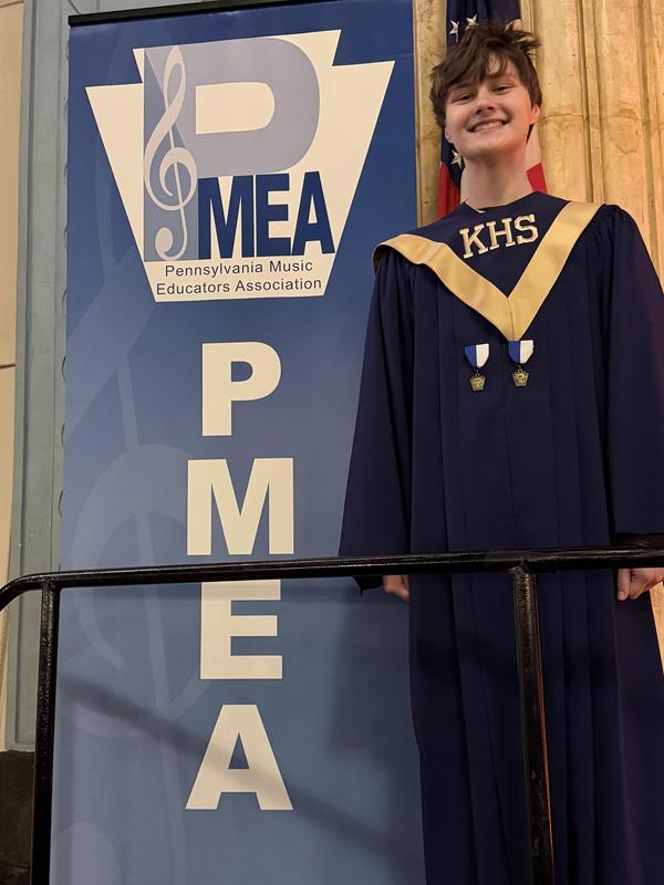 student in choral robe smiling beside PMEA sign