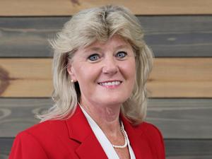 Woman with blonde hair in a red blazer, smiling against wooden background.
