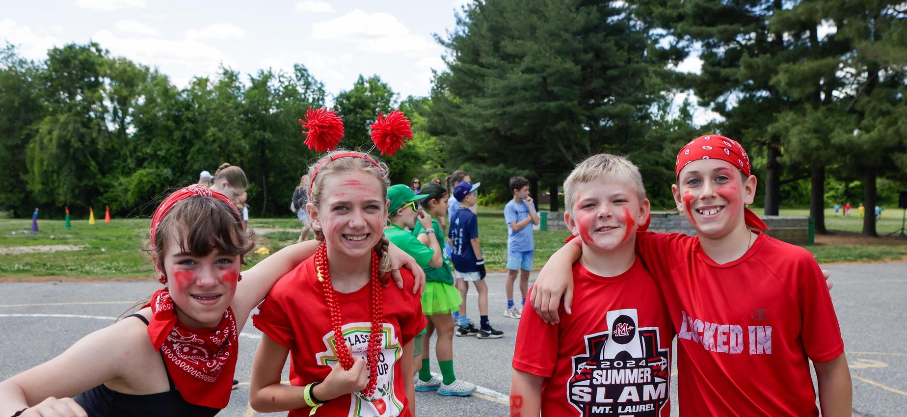 Four children dressed in red with playful faces, celebrating together outdoors.
