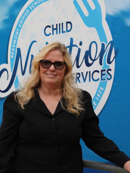 A middle age woman with blonde hair in front of the Child Nutrition Services Logo