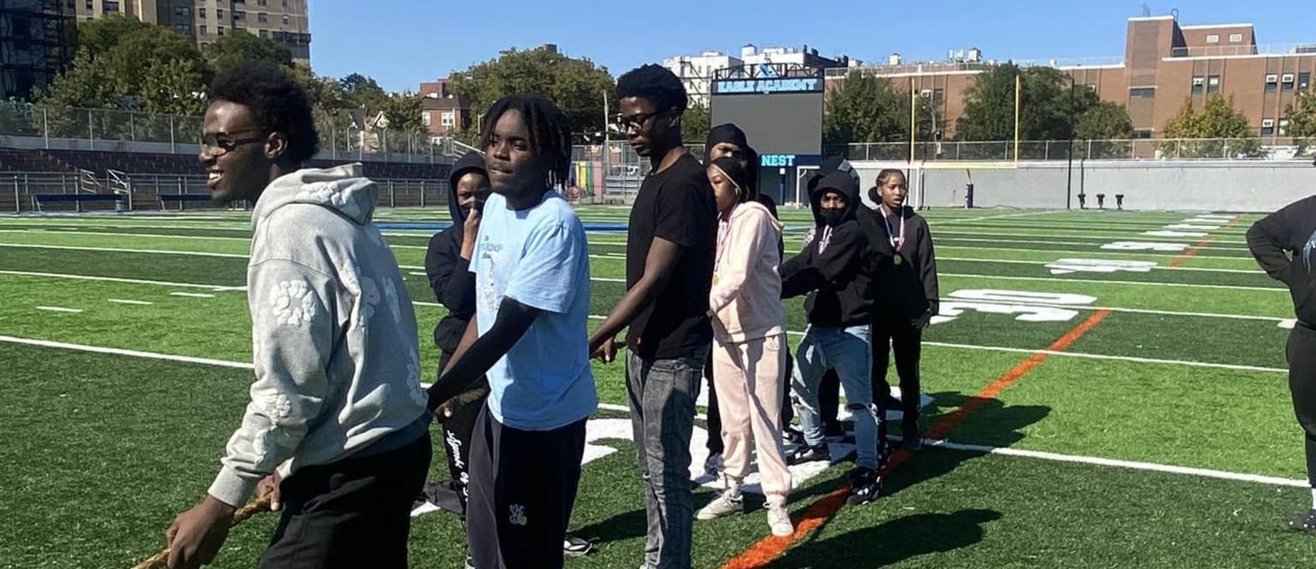Group of students engaging in a tug-of-war game on a green sports field.