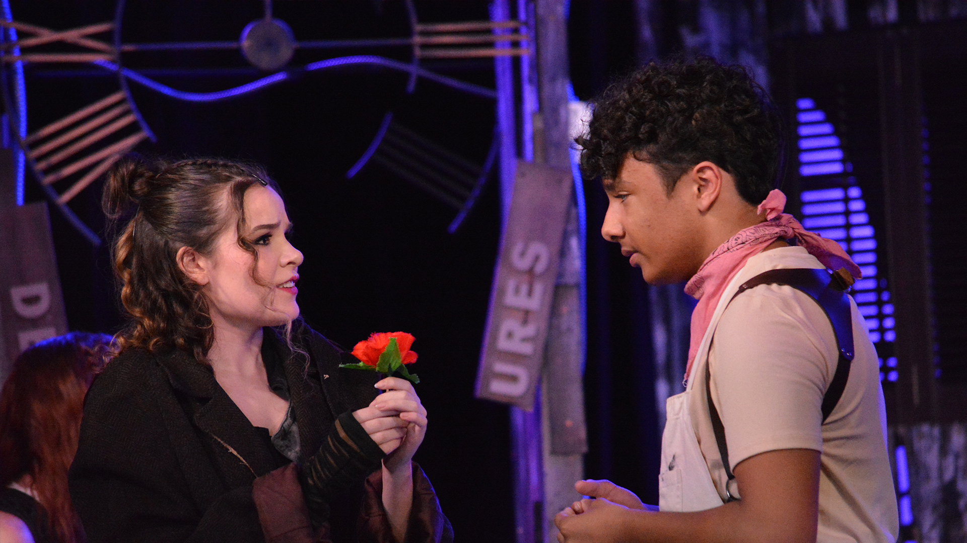 actors perform scene from Hadestown Teen Edition with Eurydice holding a red flower, facing Orpheus