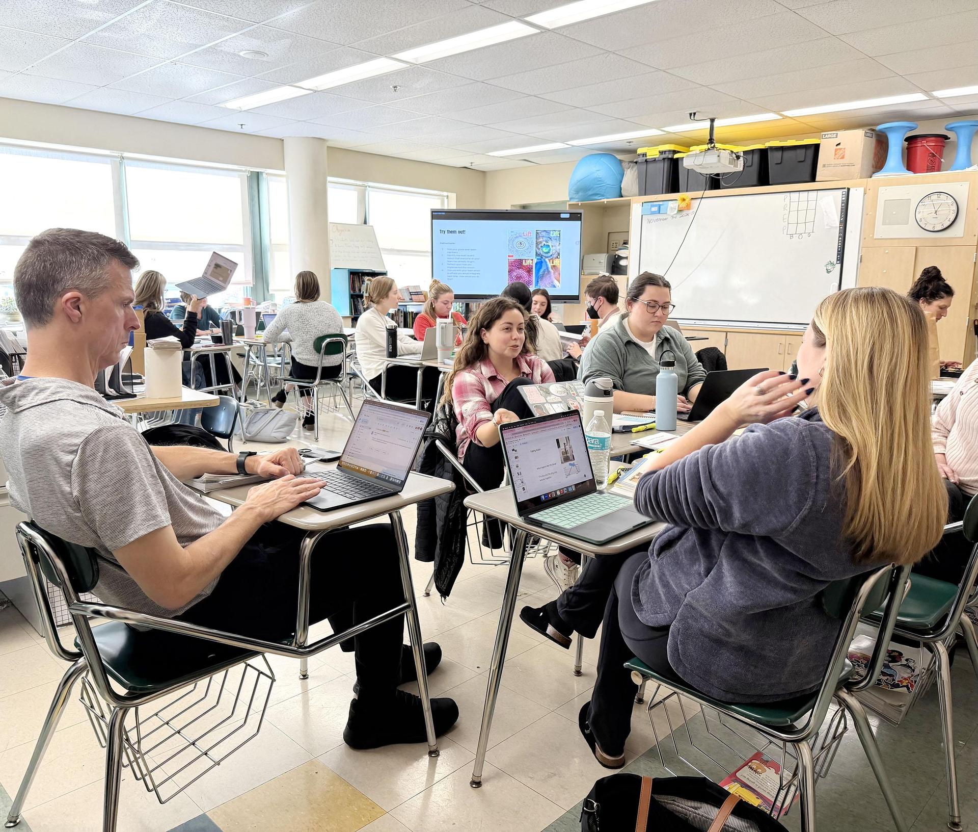 Educators working together on laptops in a classroom setting, discussing and sharing ideas.