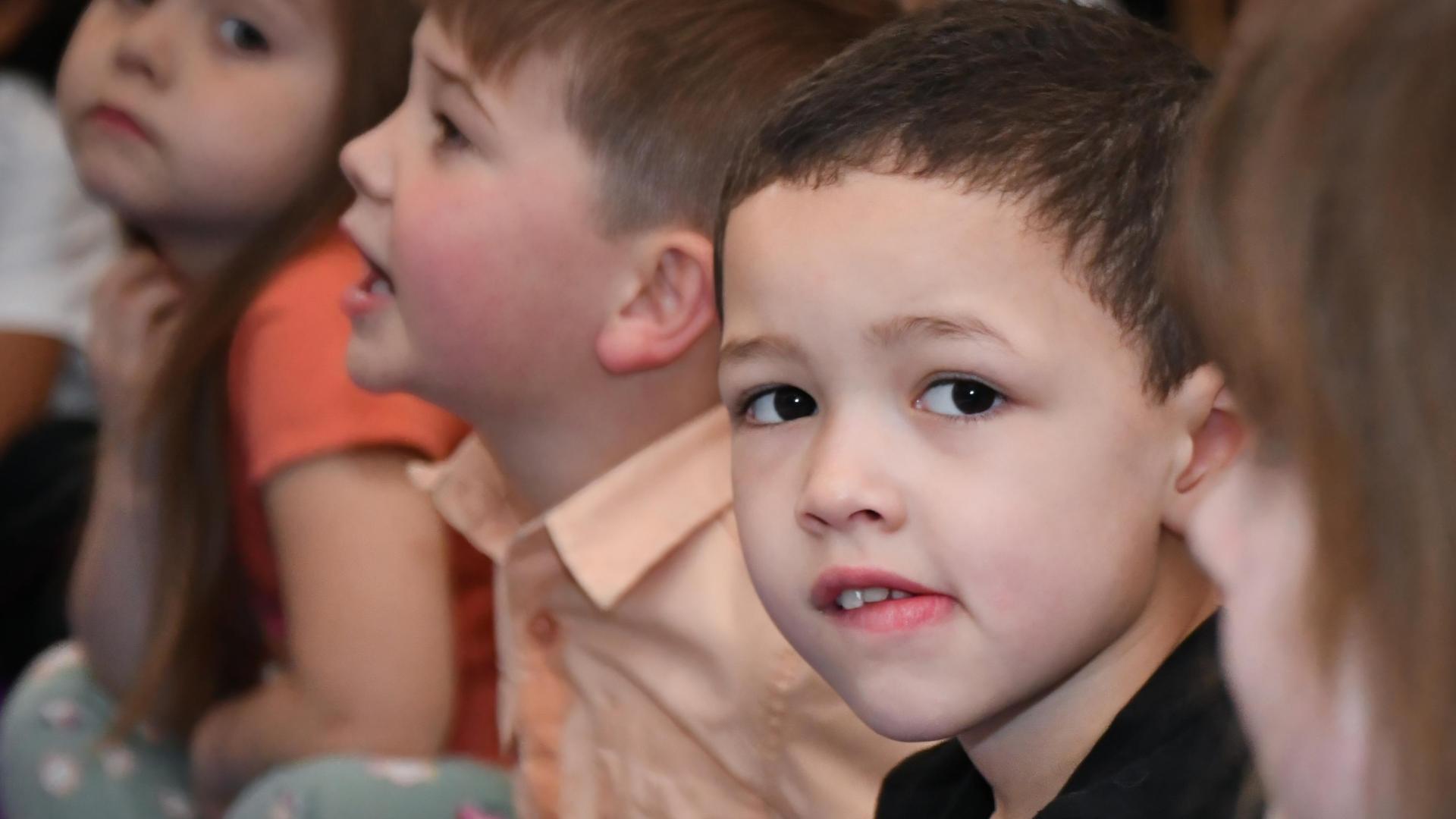 Group of children attentively watching an event, with one boy in focus.