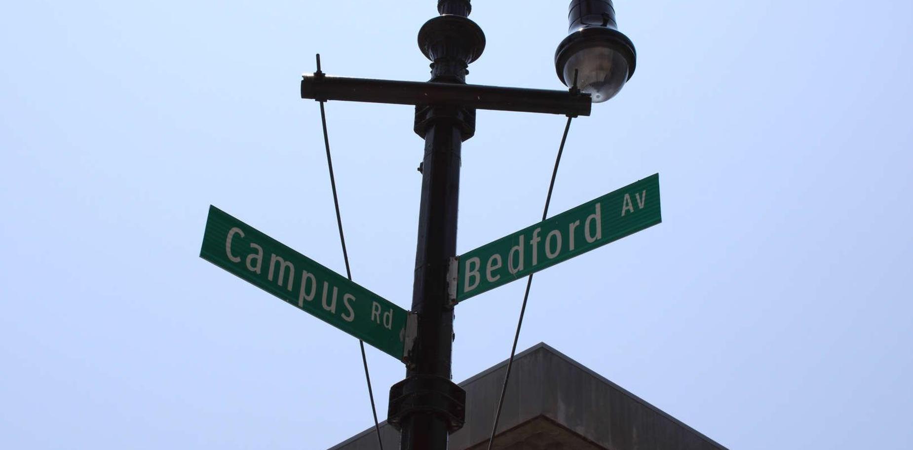 Street signs for Campus Rd and Bedford Ave against a blue sky.