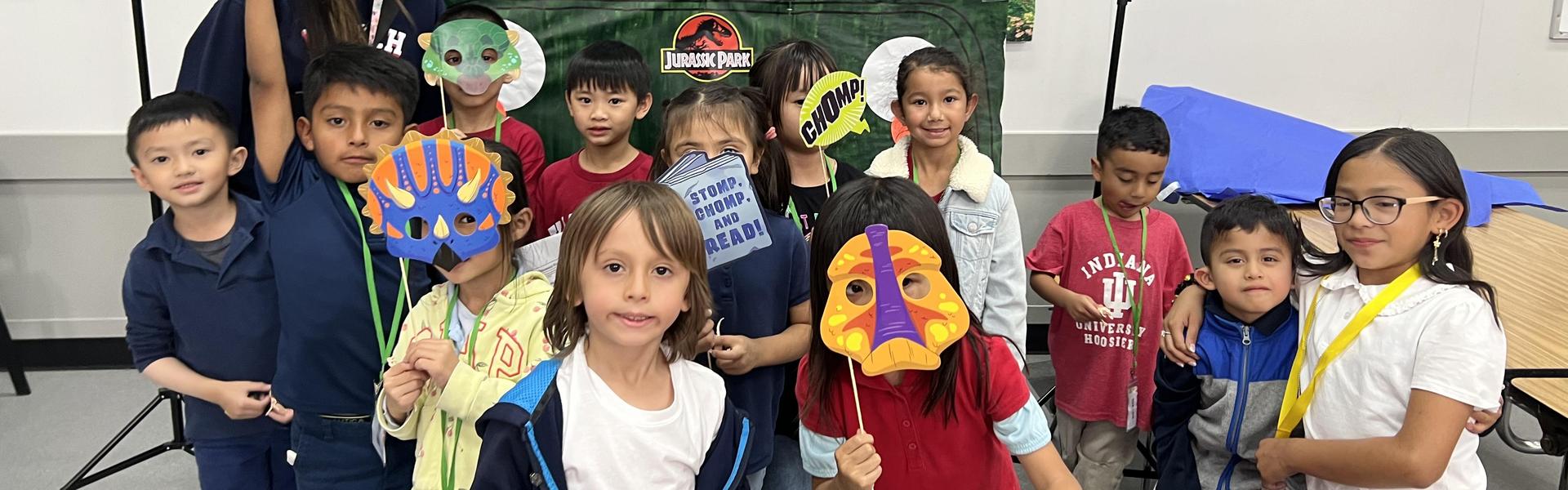 Children posing with masks in a dinosaur-themed setting.