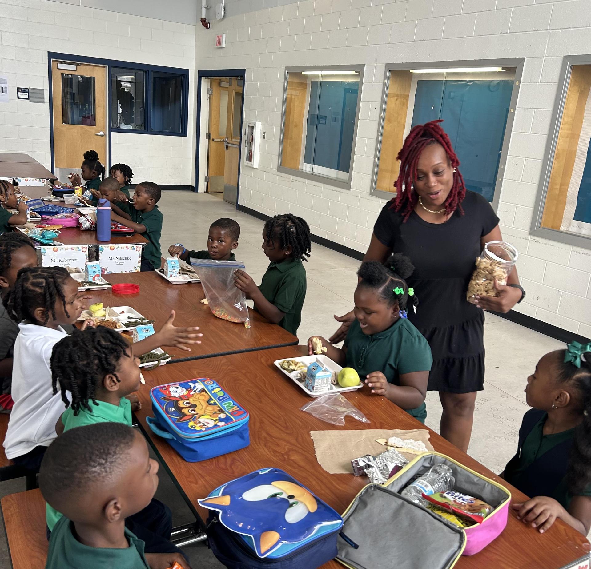 Children at a lunch table engaging with a caregiver and their meals.