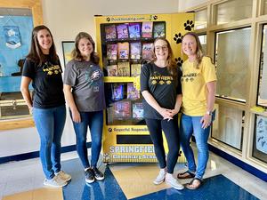 Four PTA officers standing in front of a book vending machine with a ribbon on it.