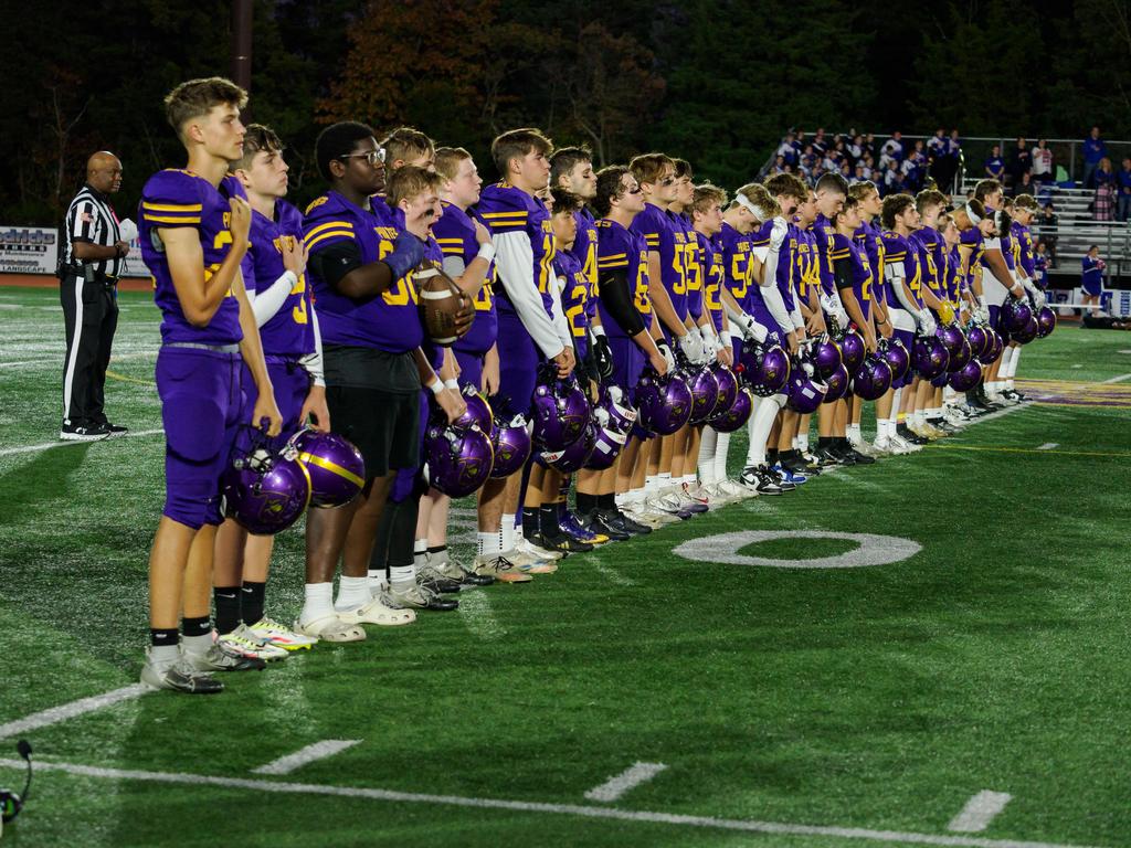 Football players in a line saluting the flag on the field before a game.