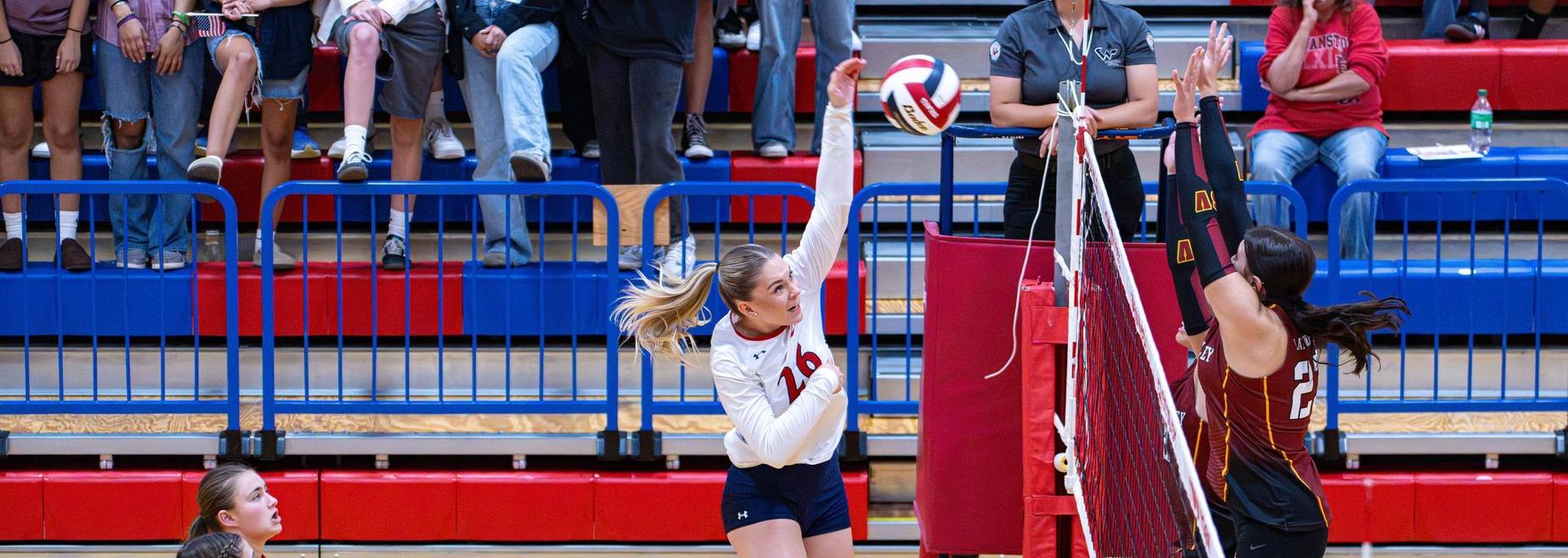 Volleyball players in action during a match with one attempting to spike the ball.