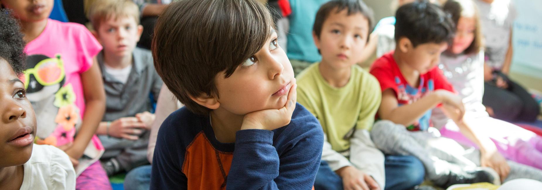 Students sitting on the rug watching the teacher