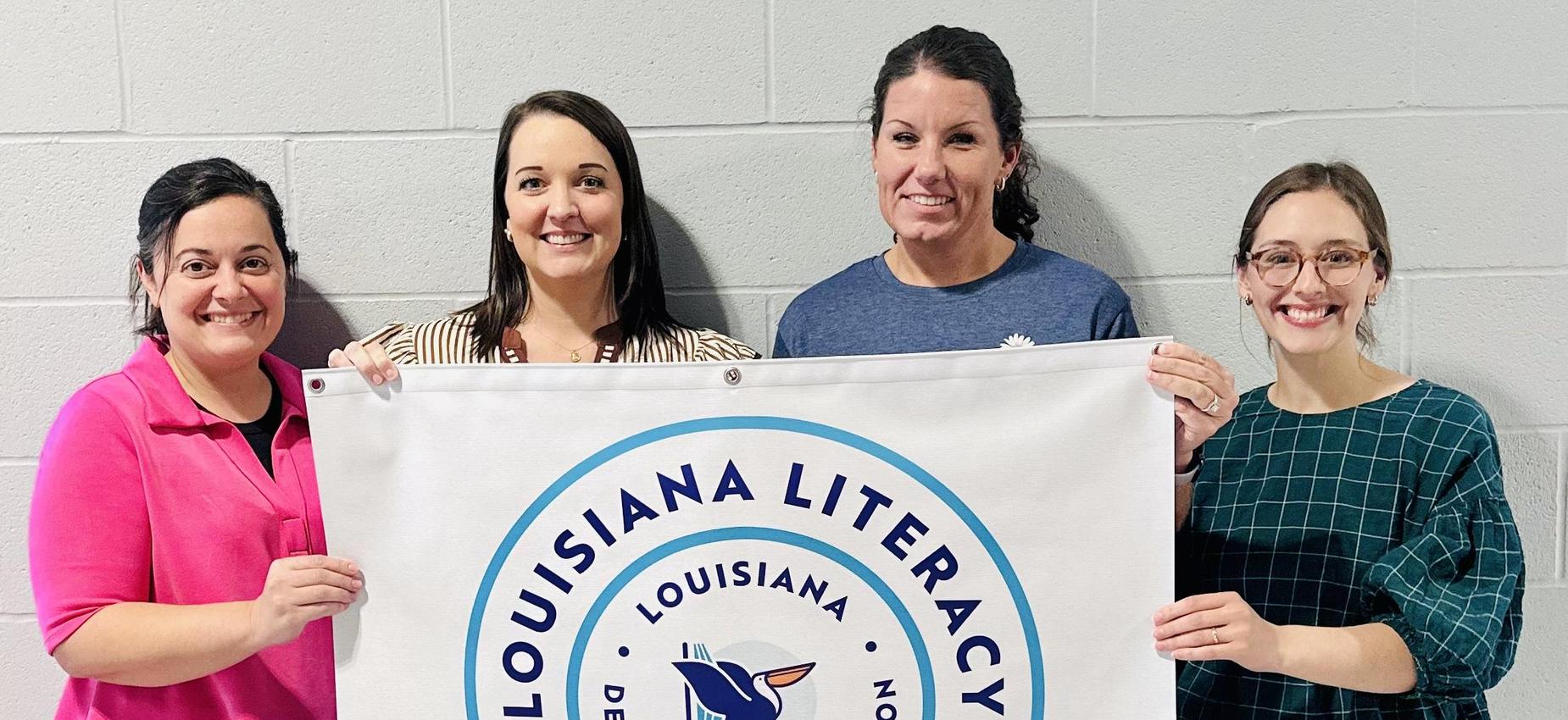 Two women displaying a banner for literacy leadership recognition in Louisiana.