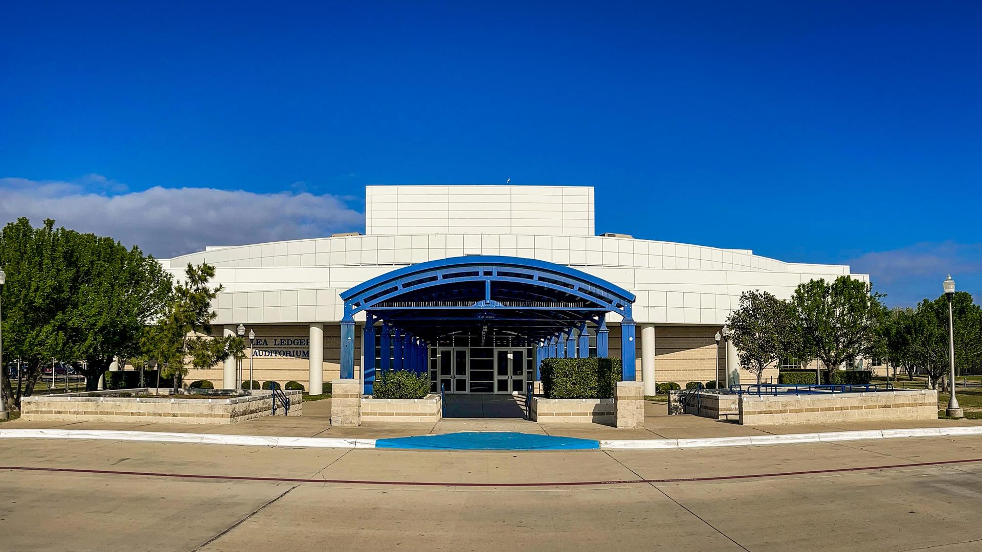 Exterior of a modern building with a blue canopy and landscaped trees.