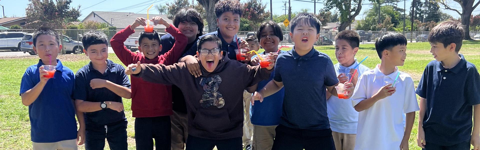 Group of kids posing joyfully outdoors with drinks, enjoying a sunny day.