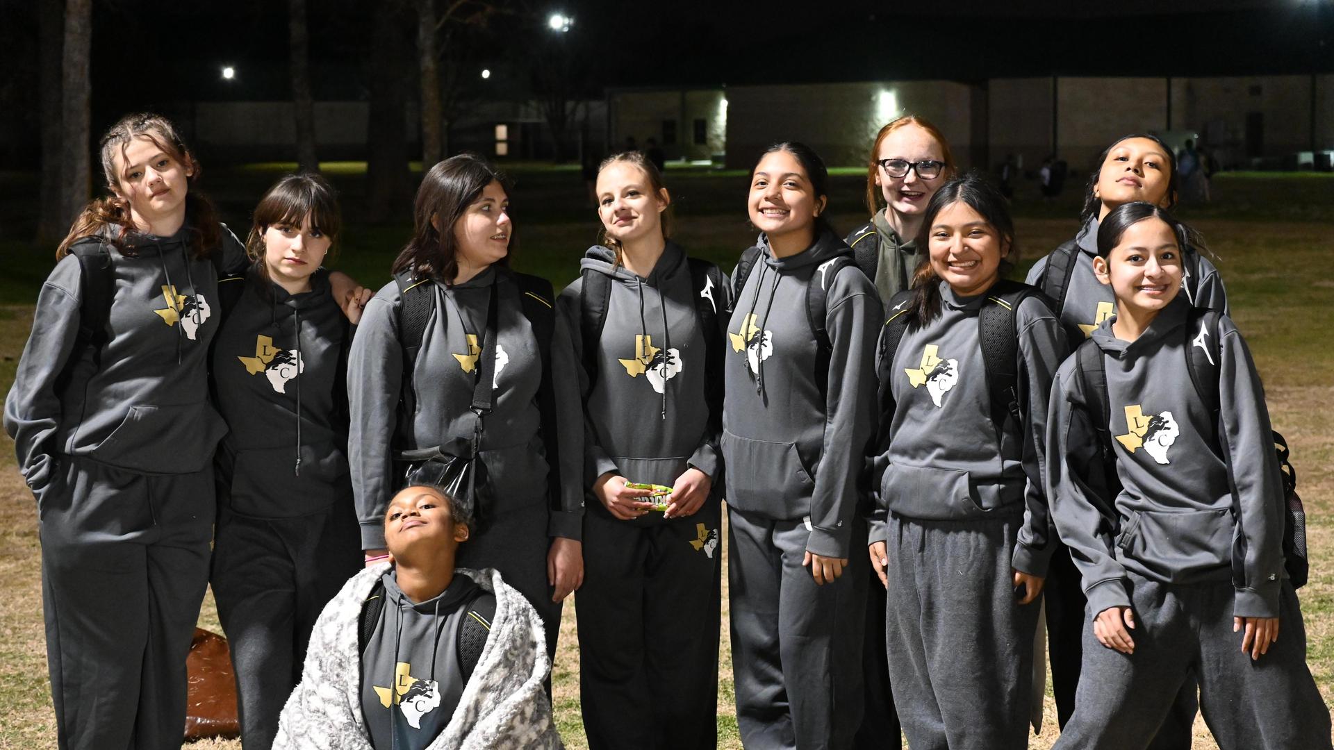 Group of young athletes in matching gray sweat suits posing together outdoors for a junior high track meet.