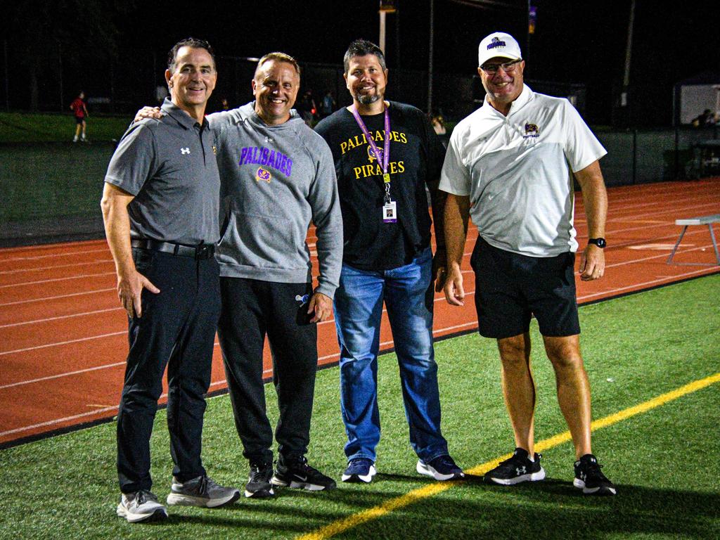 Four men posing together on a sports field, smiling at the camera.