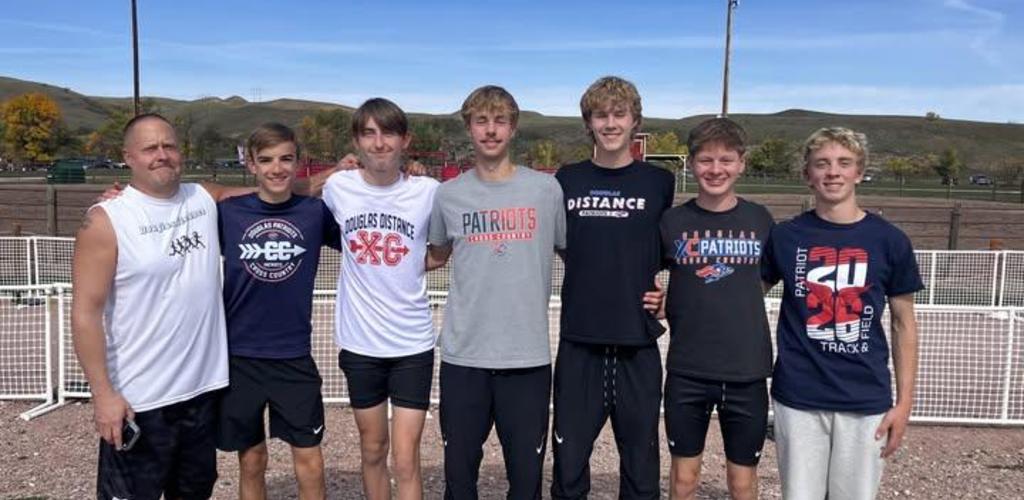 Seven male cross-country runners in team shirts pose outdoors with hills in the background.
