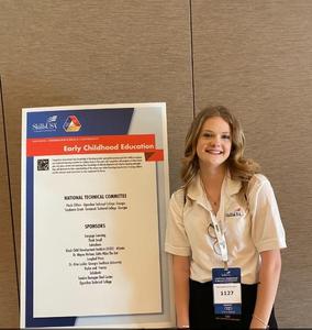 A smiling girl in front of a SkillsUSA poster.