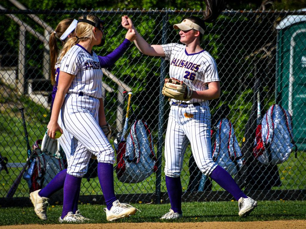 Two high school softball players giving one another a high-five.