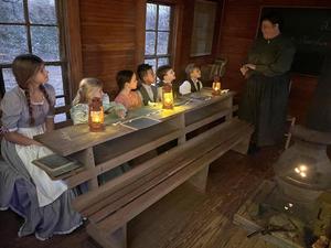 Saundra and 1st graders dressed as 19th-century pioneers in a one-room schoolhouse during a reenactment.