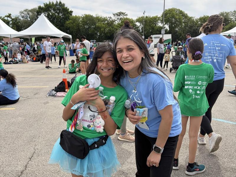 A girl and a woman smile together at an outdoor event.