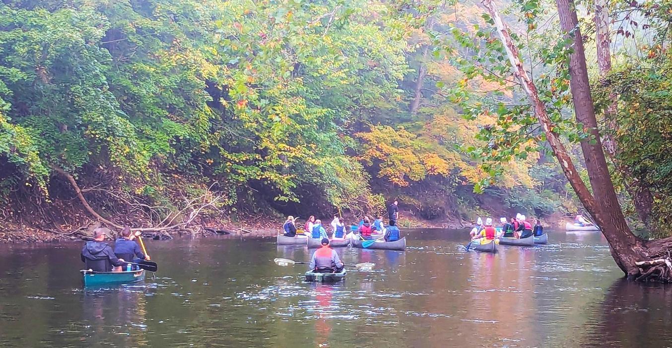 Groups of people canoeing on a calm river surrounded by autumn foliage.