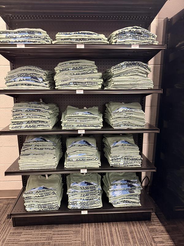 Shelves stacked with neatly folded green t-shirts featuring a design.