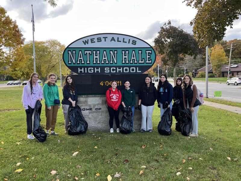 Students holding garbage bags in front of Nathan Hale High School sign.