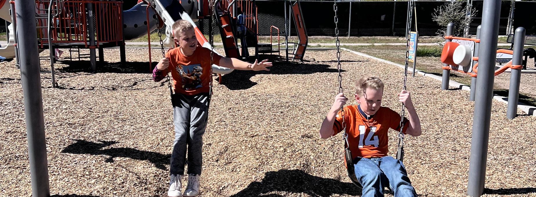 Two children swinging on a playground with one reaching out towards the other.