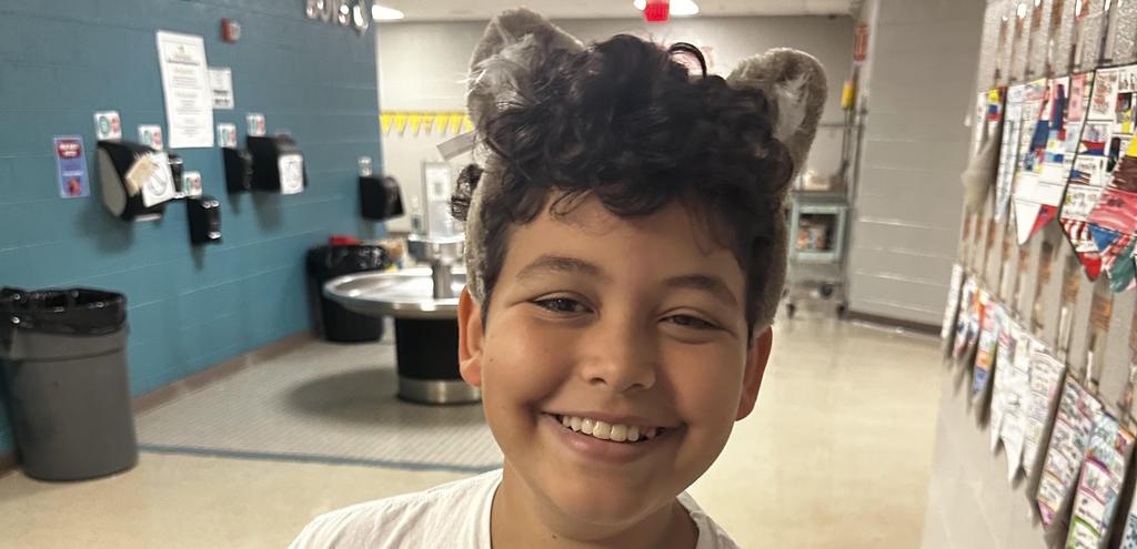 Smiling boy wearing a Pizza Planet t-shirt in a school hallway.