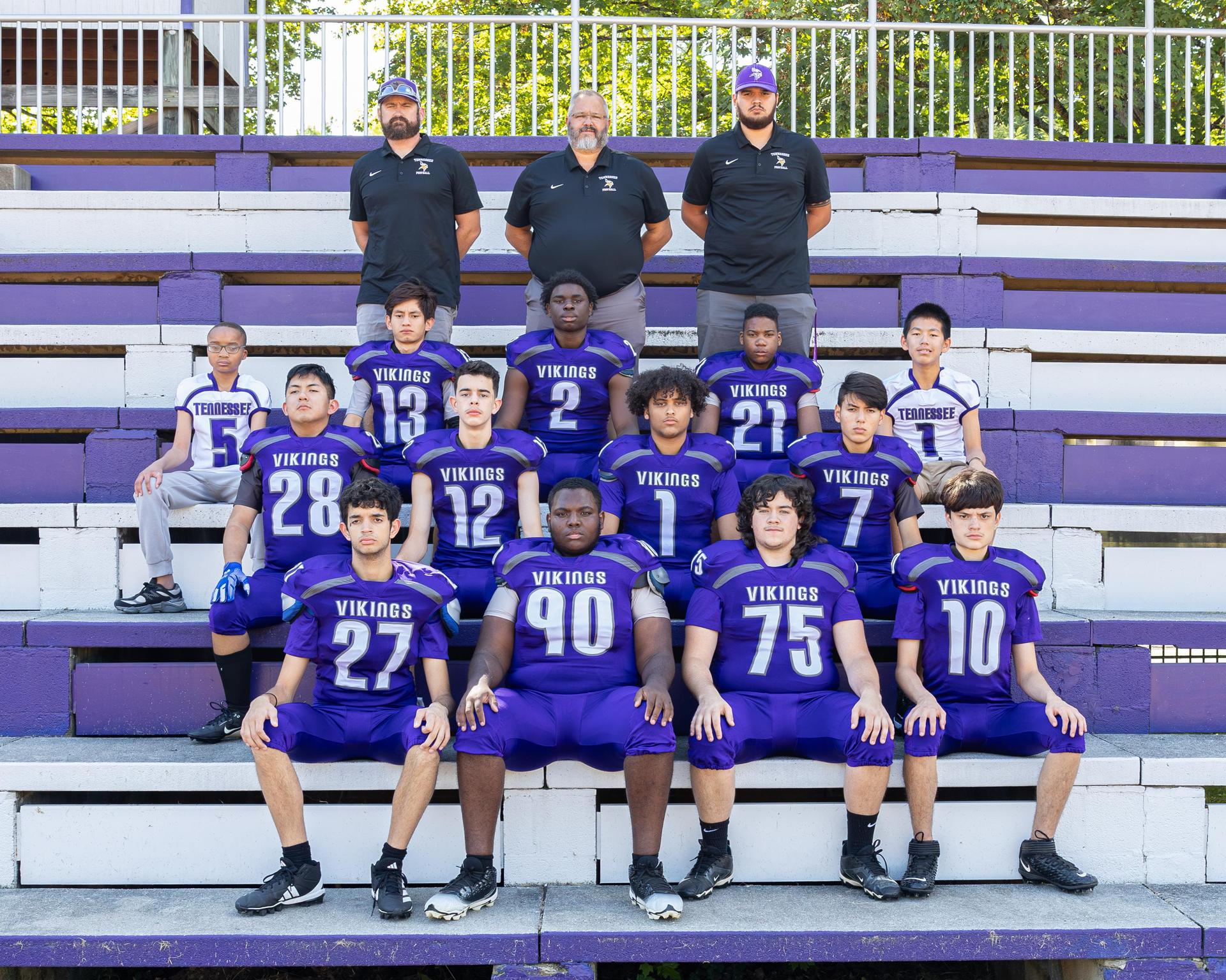 Varsity Football team picture with with team sitting on the bleachers outside at the football field
