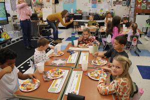 Students seated at desk eating pie