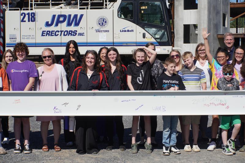 students and staff standing behind steel beam that they signed