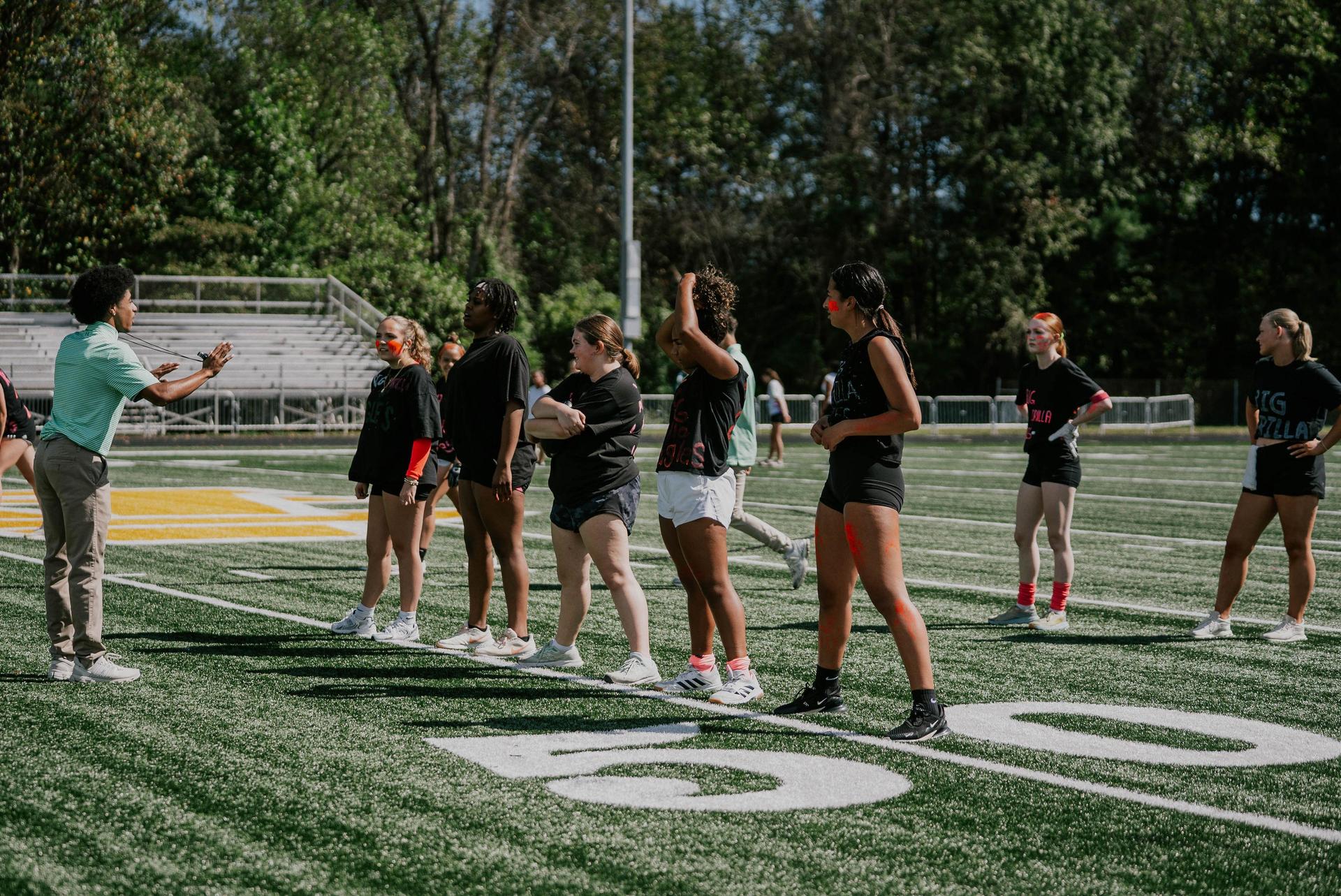 A group of female athletes listens attentively on a sports field during practice.