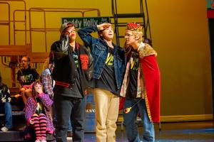 Three students on stage during godspell, acting out a scene.