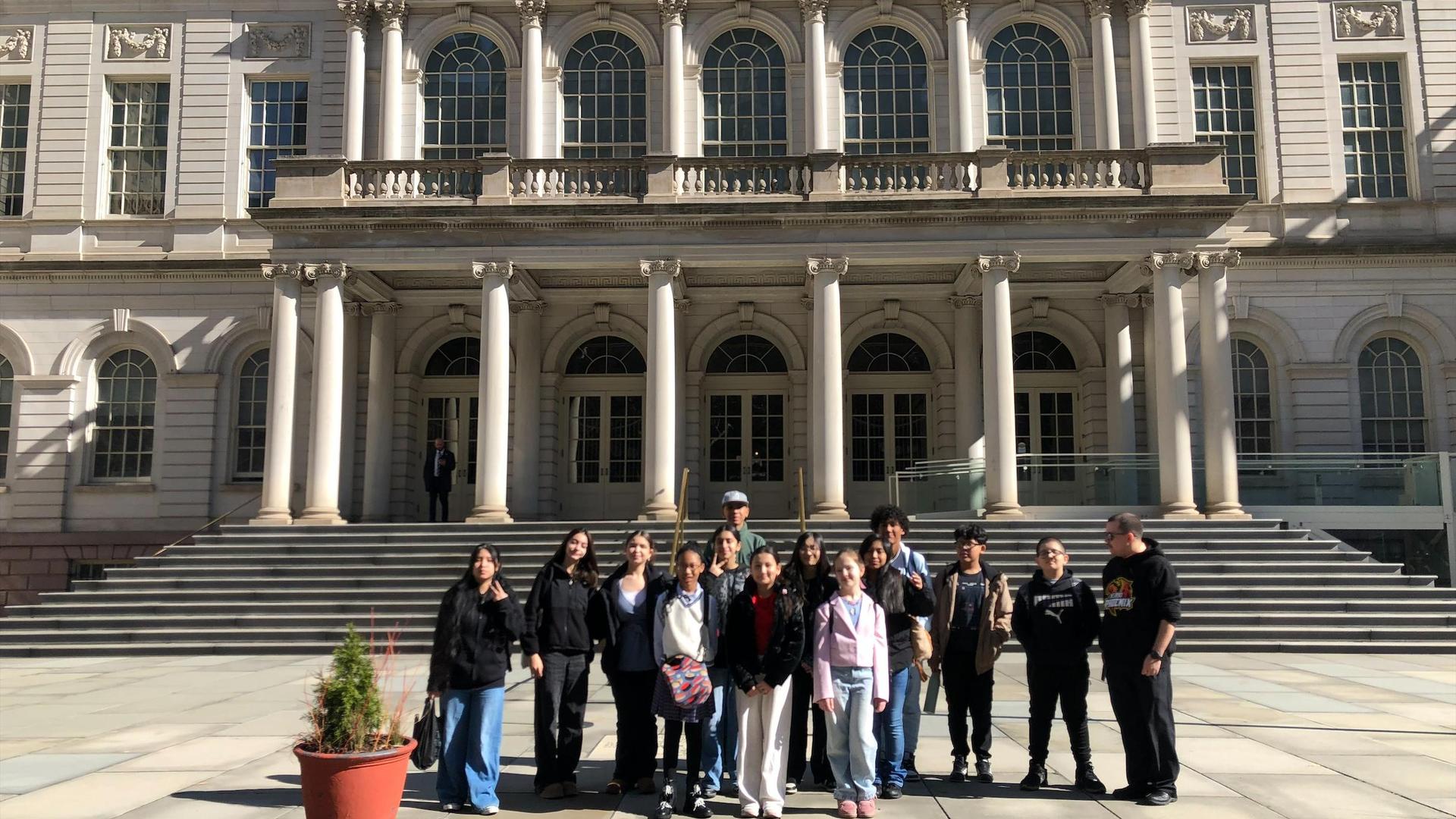 A group of people posing in front of a grand building with columns and stairs.