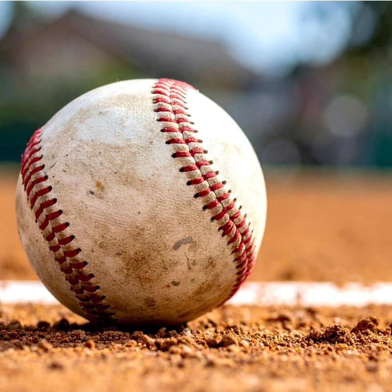 A close-up of a dirty baseball resting on a sandy field.