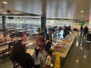 Visitors line up at a food table in a school cafeteria during an event.