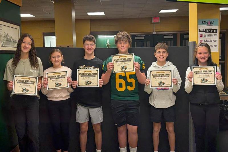 Six students holding certificates stand in a classroom