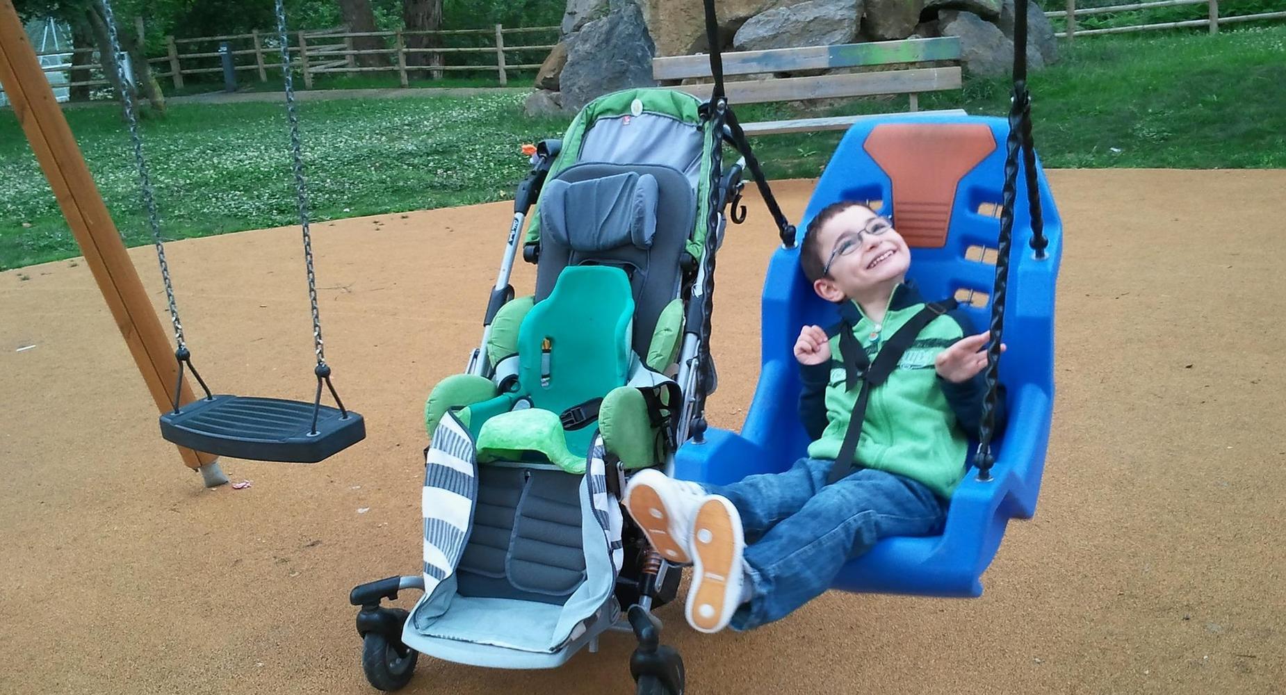 smiling boy swinging in an adapted swing next to his wheelchair