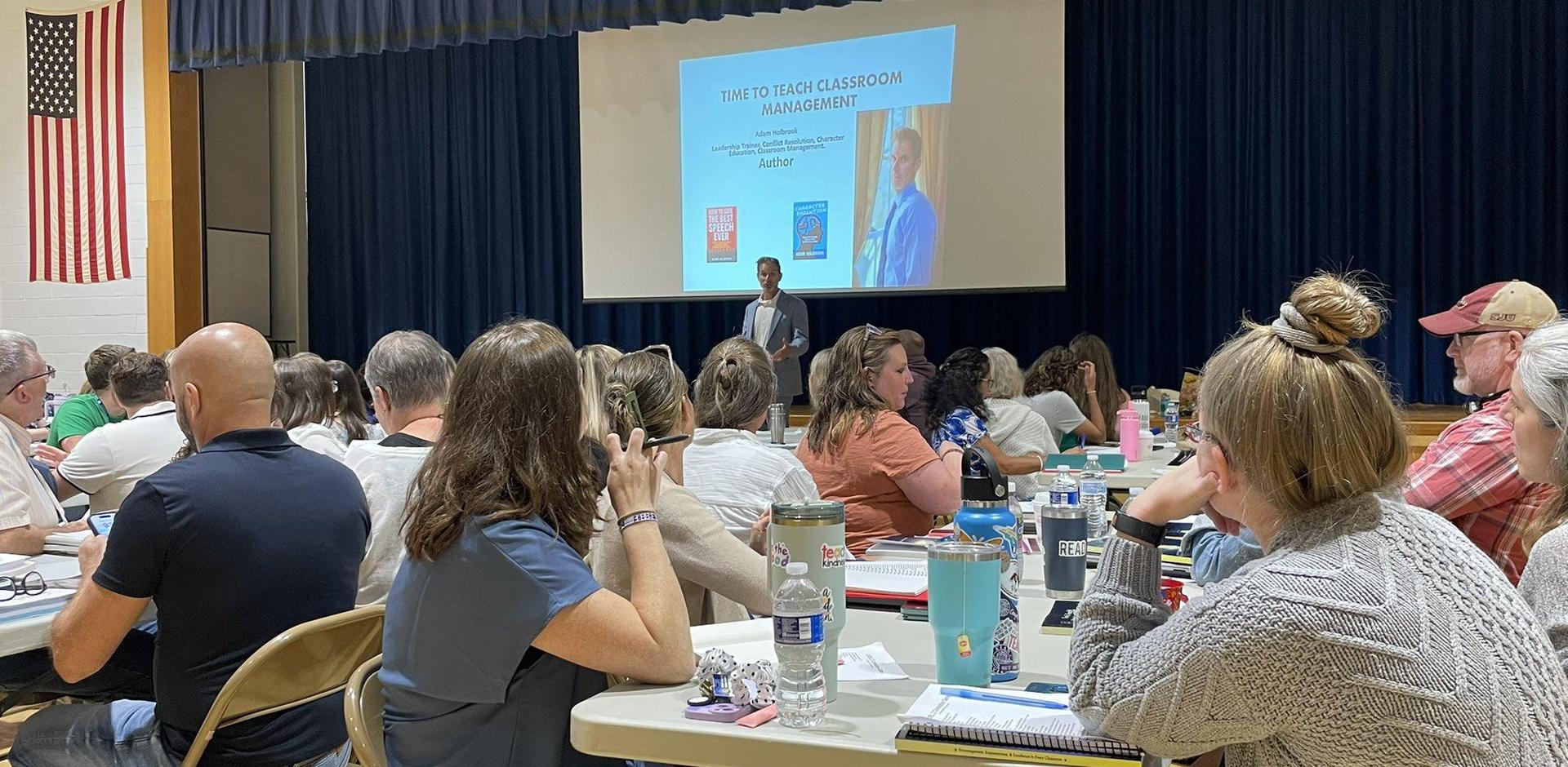 A speaker presents on classroom management to an audience in a large hall.