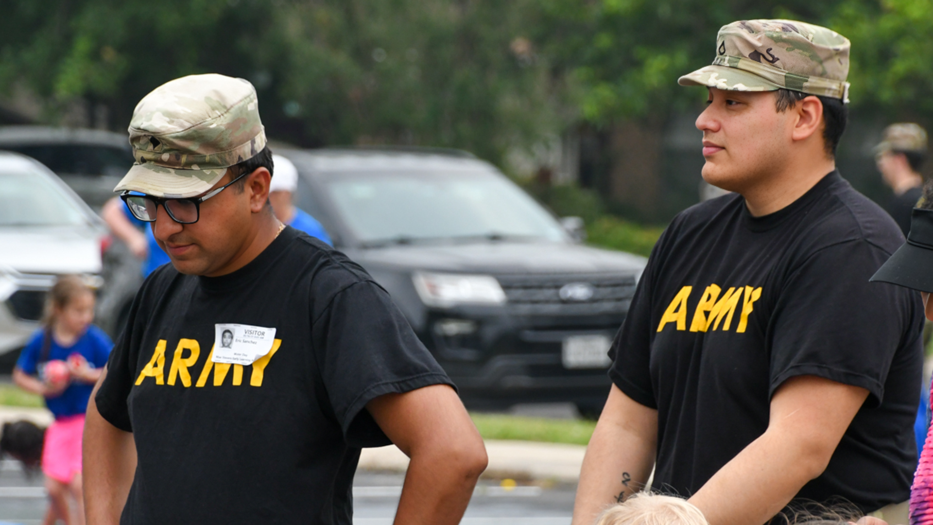 Two men in military attire, one wearing glasses, standing during an outdoor event.